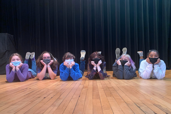 Six teenagers with masks laying on the floor with their hands raised on their chins